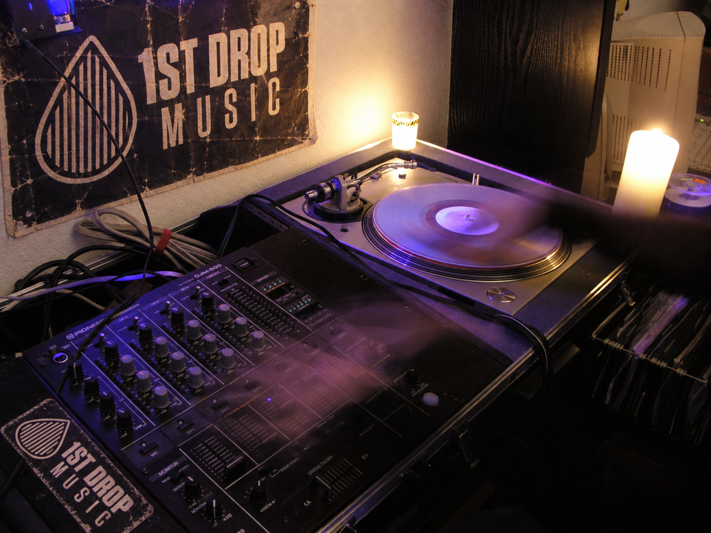 Turntable, mixer, and spinning vinyl beneath a vintage 1st Drop Music poster