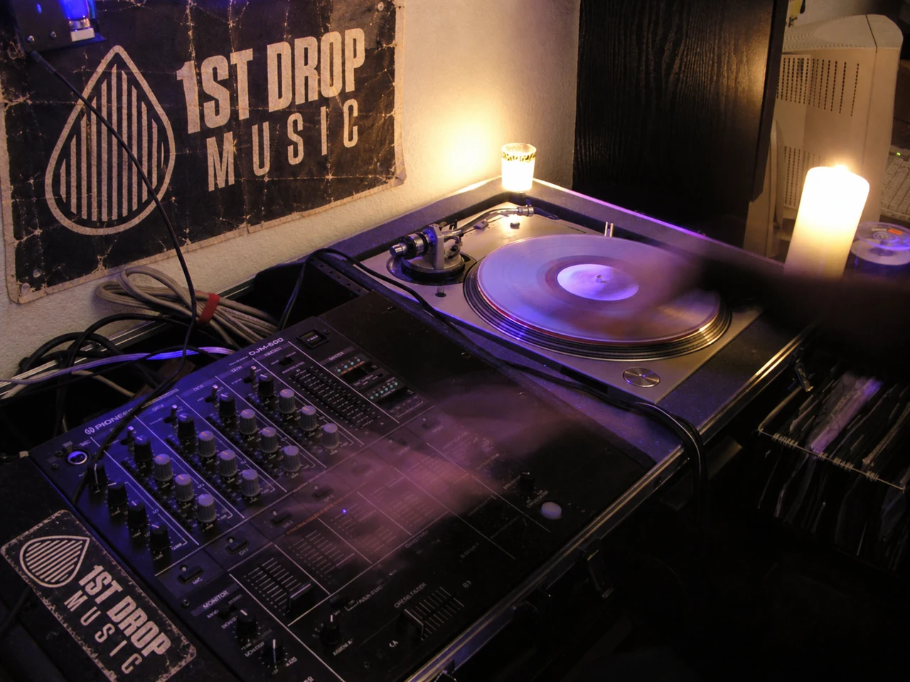 Turntable, mixer, and spinning vinyl beneath a vintage 1st Drop Music poster